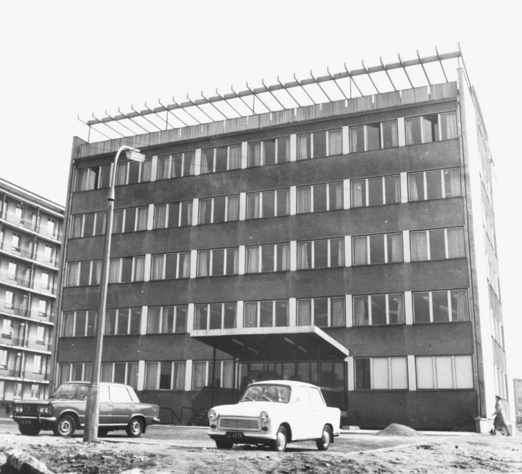 Czteropiętrowy budynek. Z przodu samoch&oacute;d. Zdjęcie czarno-białe